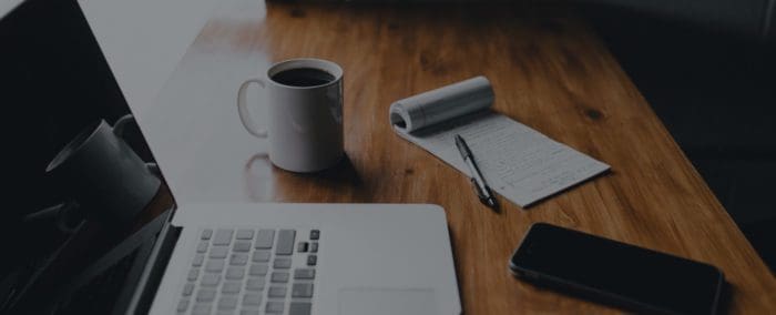 notepad next to a laptop & coffee